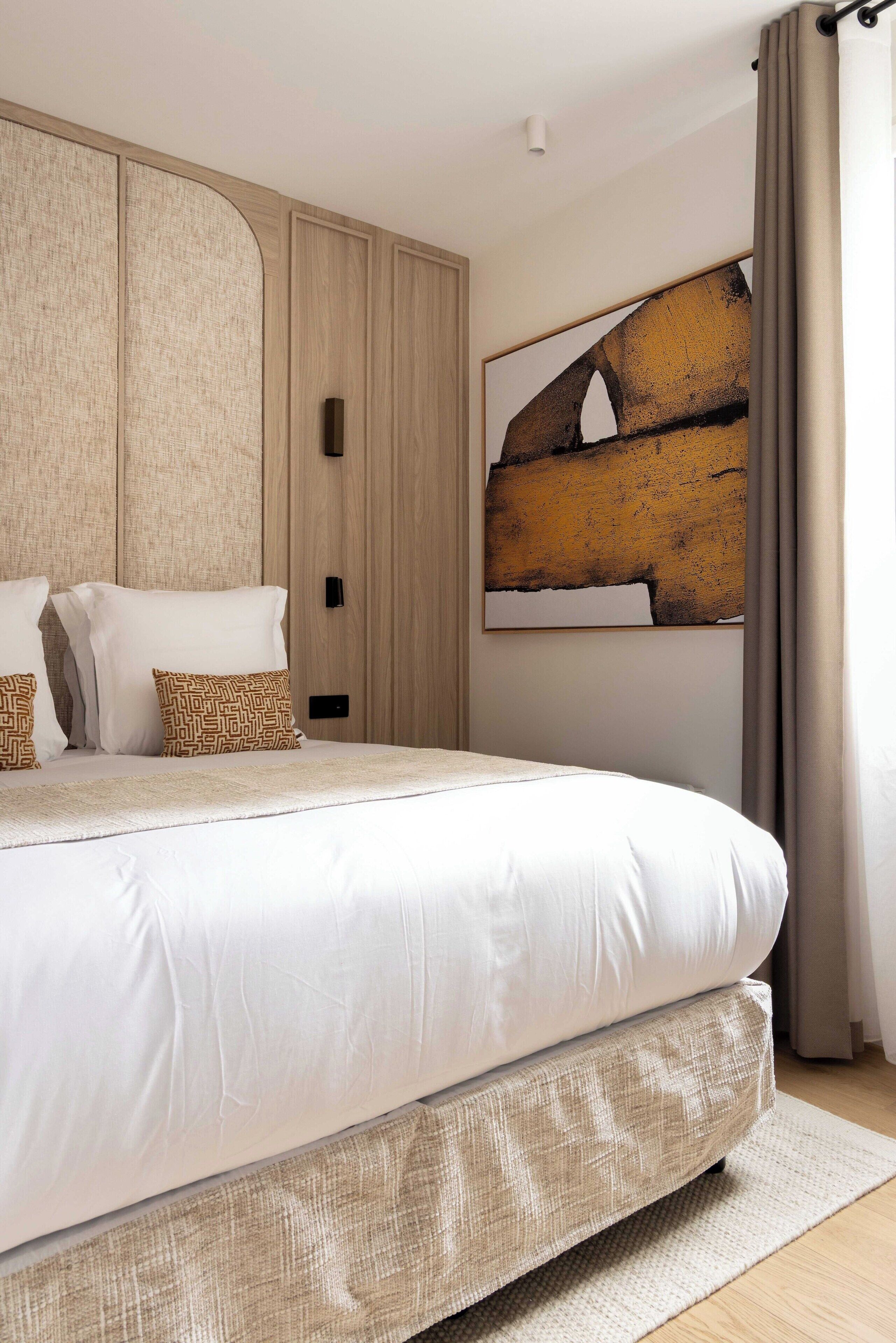 Ein modernes Schlafzimmer mit einem großen Bett, einem Bettrahmen mit Stauraum, einem an der Wand befestigten Kunstwerk und einem Fenster mit Vorhängen.