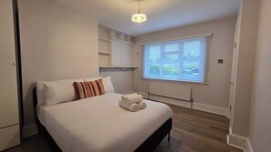 A bedroom with a bed, a radiator, a window with blinds, and built-in shelving. - Spacious Family Home 4 Beds Garden Parking (Greater London)