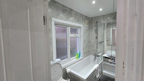Een moderne badkamer met een badkuip, douche en raam.
