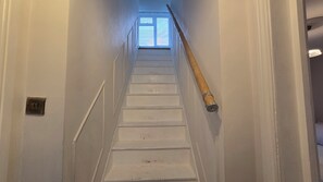 Eine Treppe mit Handlauf, einem Lichtschalter und einem Fenster am oberen Ende.
