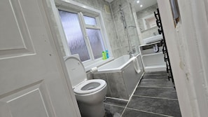 A bathroom with a toilet, a bathtub, and a window. - Spacious Family Home 4 Beds Garden Parking (Greater London)