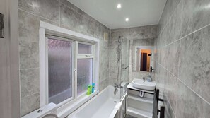A bathroom with a bathtub, a window, a shower, and a sink. - Spacious Family Home 4 Beds Garden Parking (Greater London)