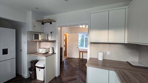 A compact kitchen with white cabinets, a microwave, a toaster, and a trash bin. - Spacious Family Home 4 Beds Garden Parking (Greater London)