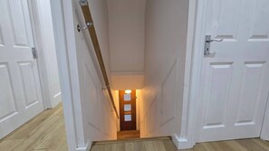 Ein schmaler Flur mit weißen Türen an beiden Seiten, einem Holzhandlauf und Licht am Ende.