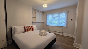 A bedroom with a bed, a radiator, a window with blinds, and a hanging light fixture. - Spacious Family Home 4 Beds Garden Parking (Greater London)