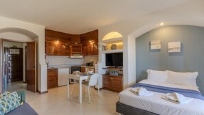 Una habitación de hotel compacta con una cama, una pequeña mesa de comedor, una kitchenette y un televisor.