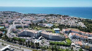 Un paisaje urbano costero con un hotel destacado, que presenta una fachada curva, varios balcones y una piscina.