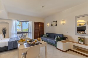 A modern hotel room with a bed, a dining area, a sofa, and a large window with a view. - #342 Cozy Studio in Belavista | Pool & Central (Albufeira)