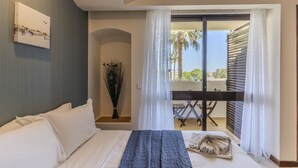 Habitación de hotel con cama, un cuadro en la pared, una planta y un balcón con mesa y sillas.