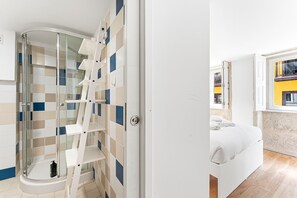 Ein Badezimmer mit Duschkabine aus Glas, einer weißen Badewanne und einer gefliesten Wand mit geometrischem Muster.