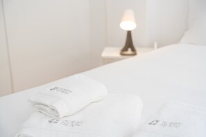 A neatly made bed with white linens and a folded towel with embossed text. - GuestReady - InPorto Building - Room 3 (Porto)