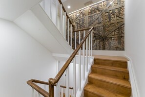 A staircase with wooden steps and white railings, leading to a room with a stone wall and a ceiling light. - GuestReady - InPorto Building - Room 3 (Porto)