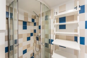 Eine Dusche mit Glastüren, ein gläserner Duschbereich und ein weißes Regal mit blauen Akzenten.