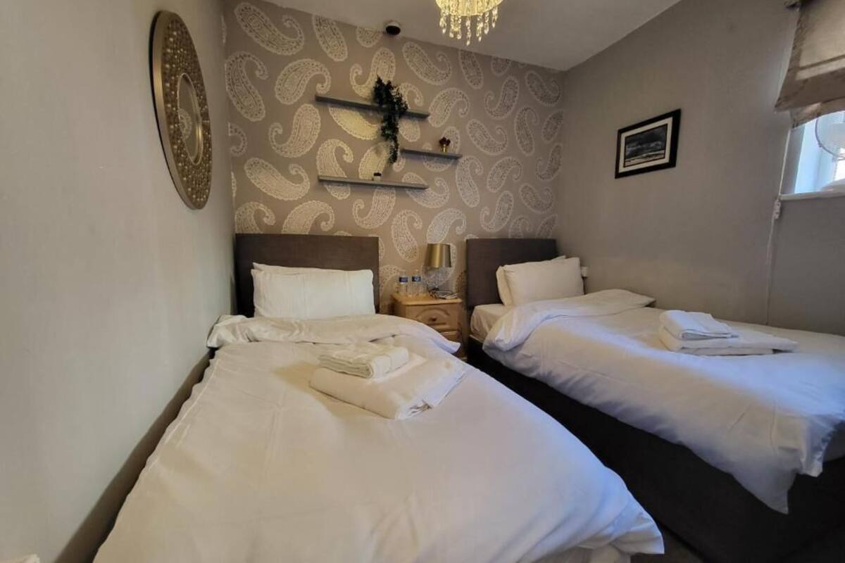 Ett hotellrum med två sängar, en kristallkrona, en vägg med mönster och en liten hylla med diverse föremål.