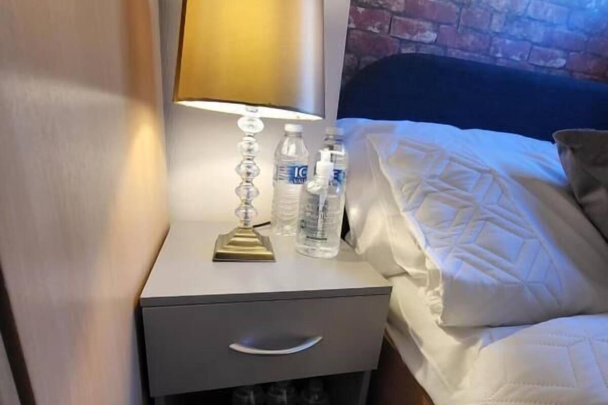 Ett hotellrum med en säng, ett nattduksbord med en lampa och en vattenflaska.