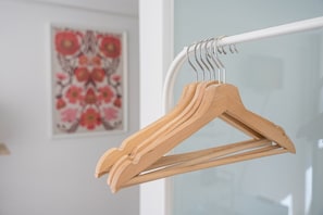 Ein Kleiderständer aus Holz mit mehreren Kleiderbügeln, eine weiße Tür und ein gerahmtes Blumenbild an der Wand.