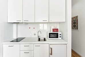 A modern kitchen with white cabinets, a sink, a microwave, and a black induction cooktop. - GuestReady - InPorto Building - Room 1 (Porto)