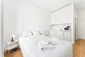 A hotel room with a bed, a nightstand, a desk, a kitchenette, and a wardrobe. - GuestReady - InPorto Building - Room 1 (Porto)