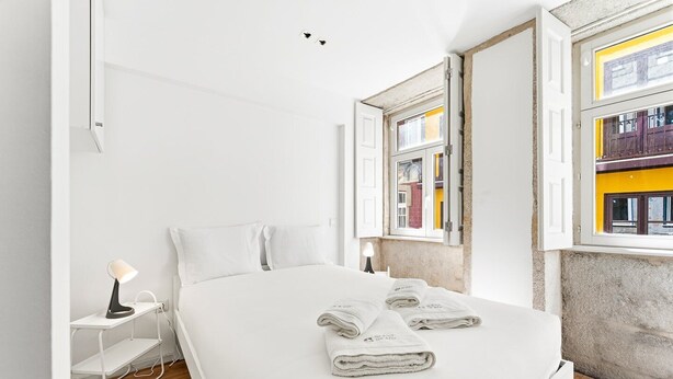 A hotel room with a bed, a desk, a lamp, and a window with a view of buildings. - GuestReady - InPorto Building - Room 2 (Porto)