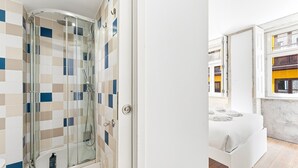 A modern bathroom with a glass shower enclosure, a white sink, and a window with a view of the city. - GuestReady - InPorto Building - Room 2 (Porto)