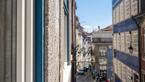 A narrow street with buildings on either side, a clear sky, and a few pedestrians. - GuestReady - InPorto Building - Room 2 (Porto)