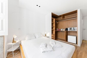 Quarto moderno com cama, mesas de cabeceira, guarda-roupa e micro-ondas.