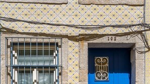 En bygning med en blå dør, nummer 102, og et vindue med metalgitter.