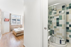 Ein Hotelzimmer mit Bett, Fenster, Dusche mit Schachbrettmuster und einem am Wand montierten Fernseher.