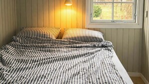 A bed with striped bedding, a bedside lamp, and a window with a view of trees. - Little oasis with large terrace and a cozy garden (Grevinge)