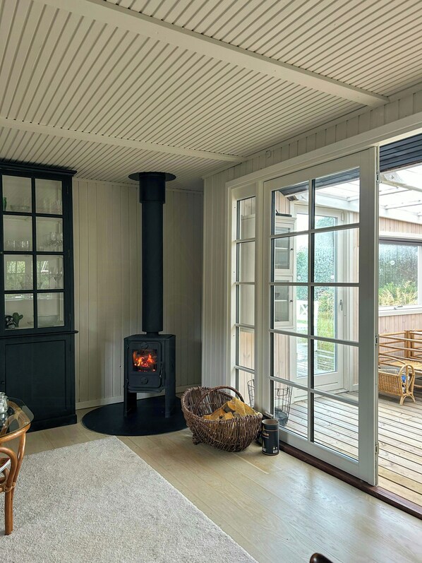 A room with a wood-burning stove, a wicker basket, and a glass cabinet. - Little oasis with large terrace and a cozy garden (Grevinge)