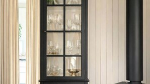 A living room with a black cabinet with glass doors, a black wood-burning stove, a round wooden table with a candle, and a white rug. - Little oasis with large terrace and a cozy garden (Grevinge)