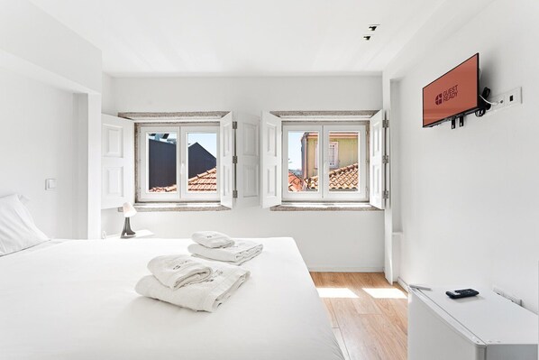 A modern hotel room with a bed, two windows, a TV, and a 'GUEST READY' sign. - GuestReady - InPorto Building - Room 6 (Porto)