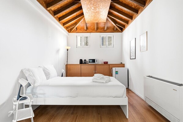 Ein Schlafzimmer mit Holzboden, einem Bett, einer kleinen Küchenzeile und einer Heizung.