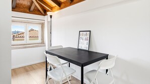 A room with a dark wooden table, white chairs, a framed picture, and a window with a view of buildings. - GuestReady - InPorto Building - Room 7 (Porto)