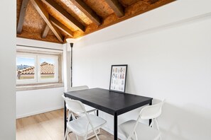 Ein Zimmer mit einem dunklen Holztisch, weißen Stühlen, einem gerahmten Bild und einem Fenster mit Blick auf Gebäude.