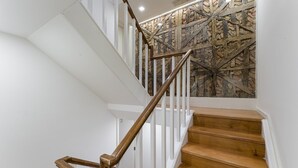 A staircase with wooden steps and white railings, leading to a room with a stone wall and a ceiling light. - GuestReady - InPorto Building - Room 7 (Porto)