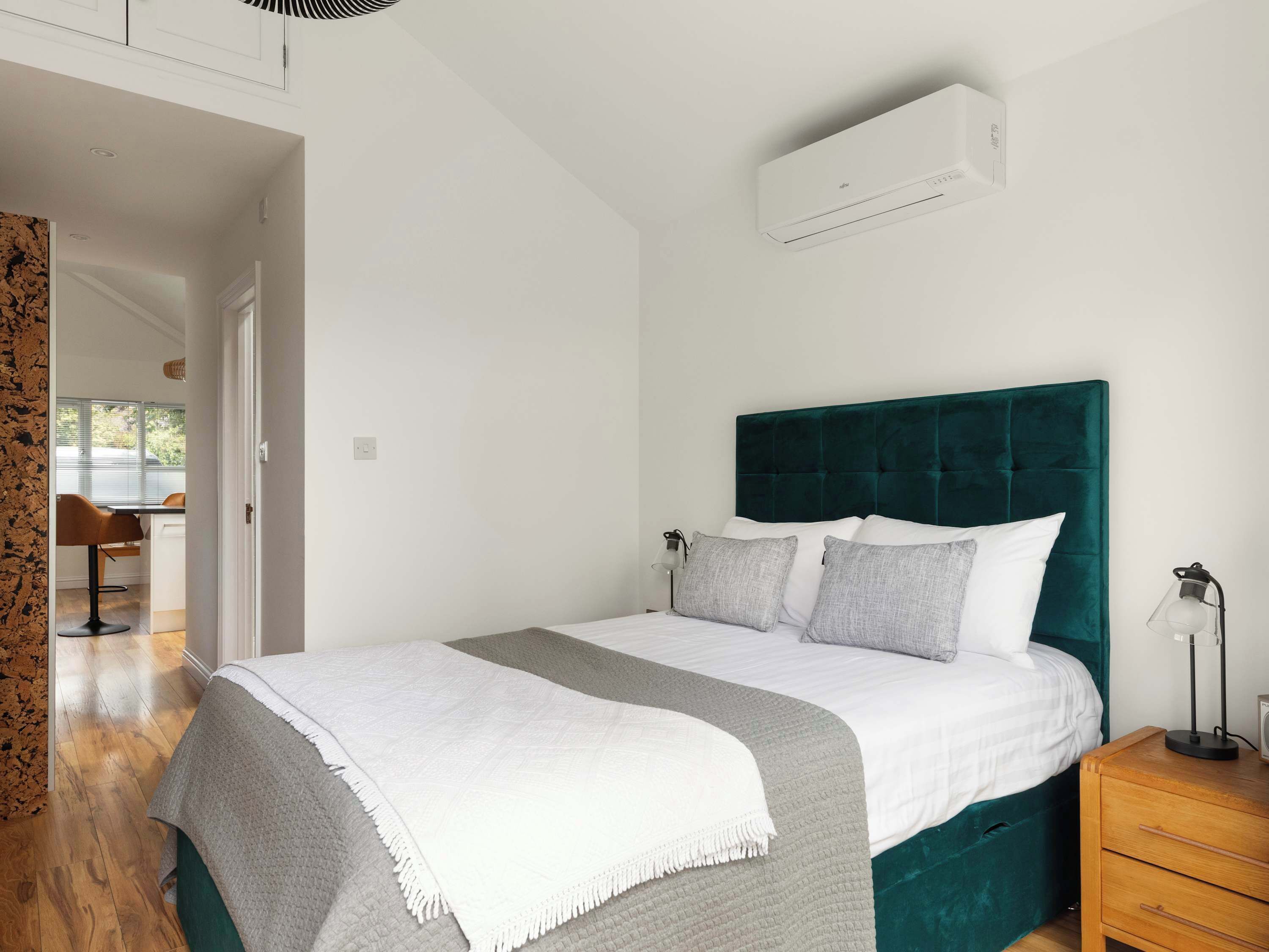Een slaapkamer met een bed, een nachtkastje, een lamp en een airconditioning.