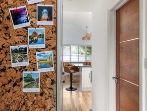 Eine Pinnwand mit angehefteten Reisefotos, ein Essbereich mit Tisch und Stühlen sowie eine Holztür.