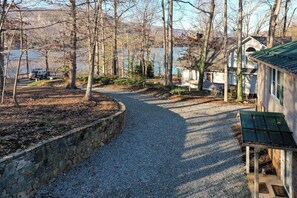 Ein Kiesweg führt zu einem Haus mit einem begrünten Dach, umgeben von Bäumen und einem Gewässer im Hintergrund.