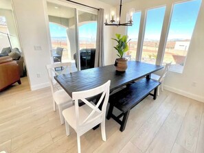 A dining area with a dark wooden table, white chairs, and a chandelier. - Paseos Pool Oasis | Outdoor Pool & Hot Tub (Washington)