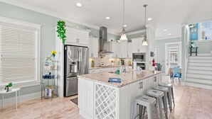 A modern kitchen with white cabinetry, a central island, stainless steel appliances, and pendant lighting. - Sea Haven (Navarre)