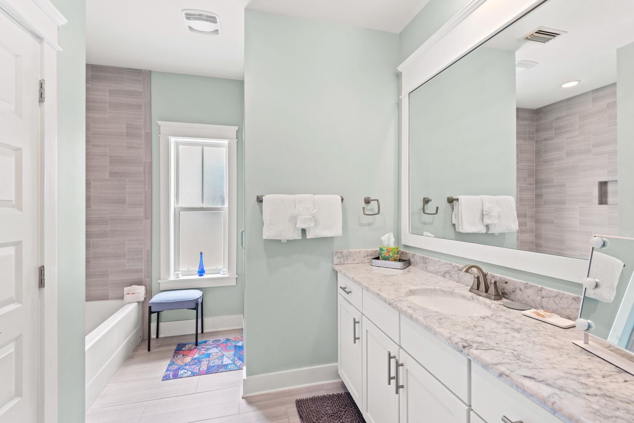 A bathroom with a bathtub, a large mirror, and a vanity with a sink.