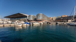 Un port de plaisance avec des bateaux amarrés, un bâtiment moderne doté d’un toit plat et une structure incurvée agrémentée de nombreux balcons.