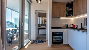 Une cuisine moderne dotée d’un four encastré, un coin repas avec une table et des chaises, et une porte-fenêtre coulissante donnant sur un espace extérieur.