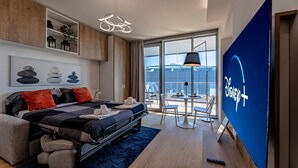 Une chambre d’hôtel moderne équipée d’un lit, d’un bureau, d’une chaise, d’une grande fenêtre et d’un panneau indiquant la présence de Disney+.
