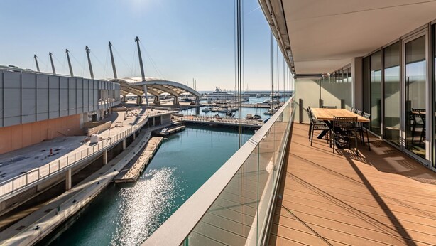 Une terrasse moderne offrant une vue sur un port de plaisance, une piscine et un espace repas avec tables et chaises.