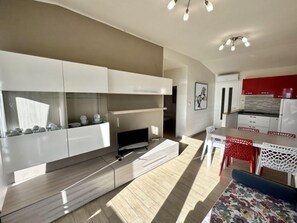 A modern kitchen with white cabinetry, a dining area with a table and chairs, and a red accent wall. - Seafront Flat With Stunning Views (San Michele al Tagliamento)