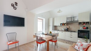 Une cuisine moderne avec un coin repas, un téléviseur à écran plat fixé au mur et un canapé agrémenté d’un coussin à motifs floraux.