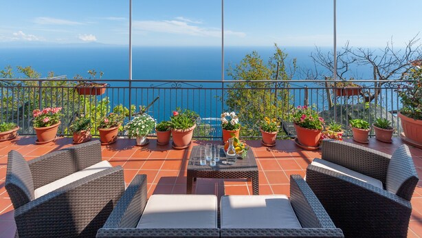 Une terrasse dotée de meubles en osier, de plantes en pot et offrant une vue sur la mer.