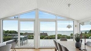 Un espace de restauration moderne, doté d’une grande table et de chaises, ainsi que de larges fenêtres offrant une vue sur la mer et le paysage environnant.